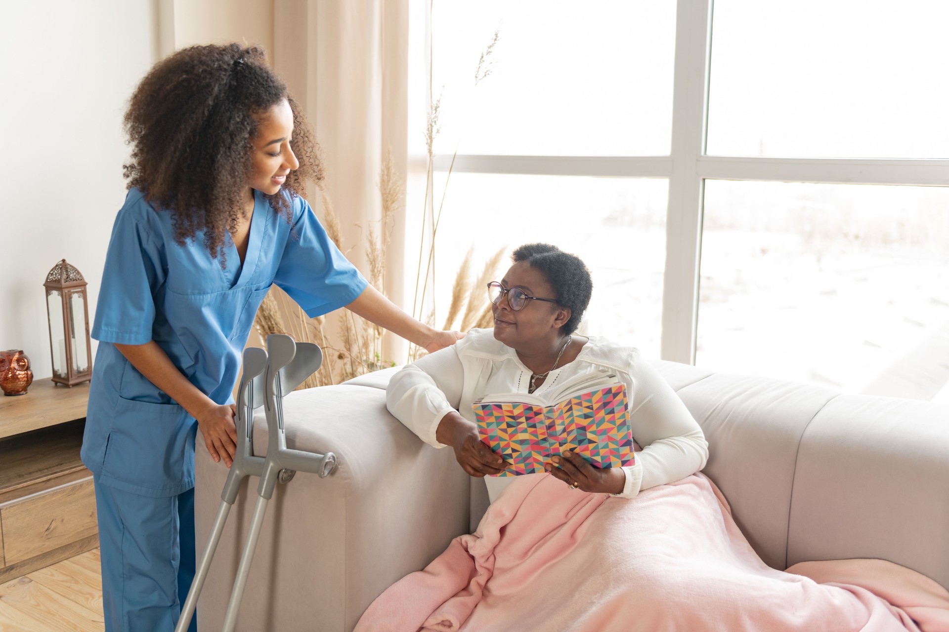 Woman with leg injury lying on sofa and talking to pleasant nurse